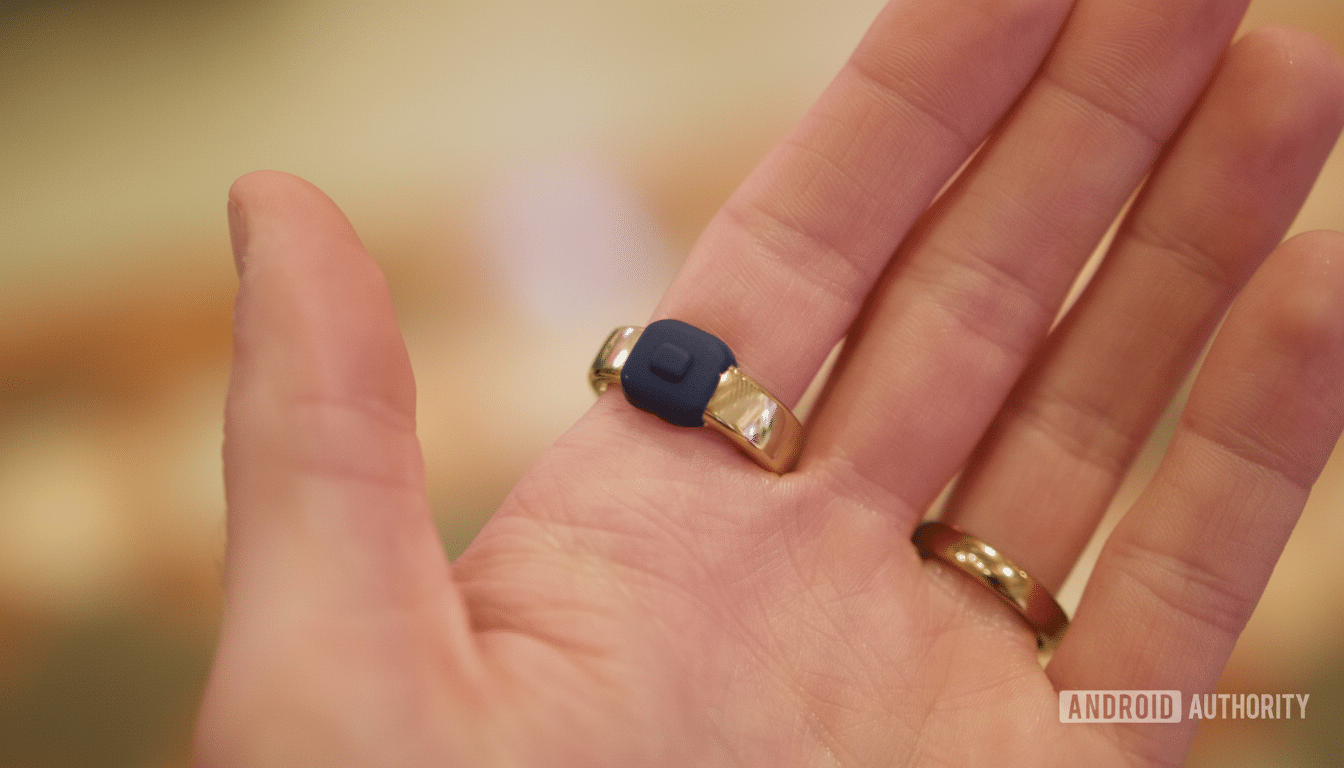 A hand wearing a gold ring with a blue square top, and another plain gold ring on an adjacent finger.
