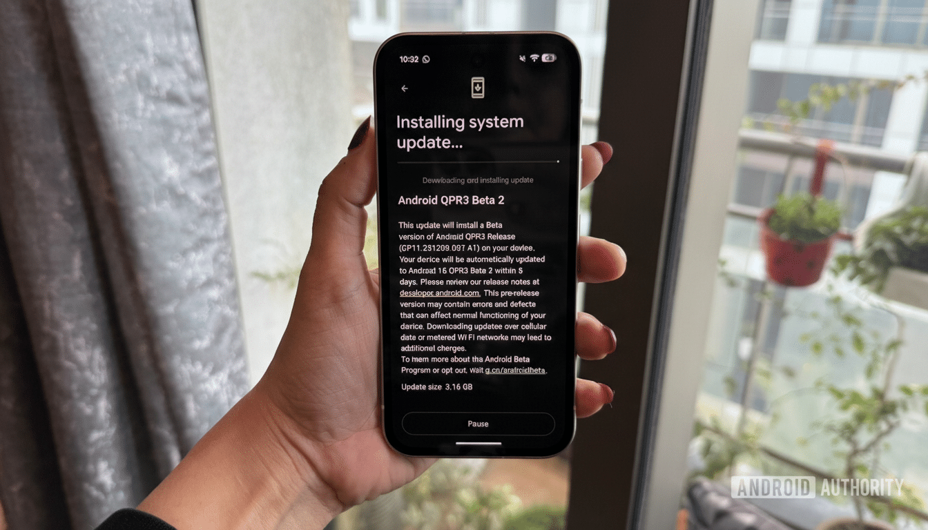 A hand holding a smartphone displaying an Installing system update... screen for Android QPR3 Beta 2.