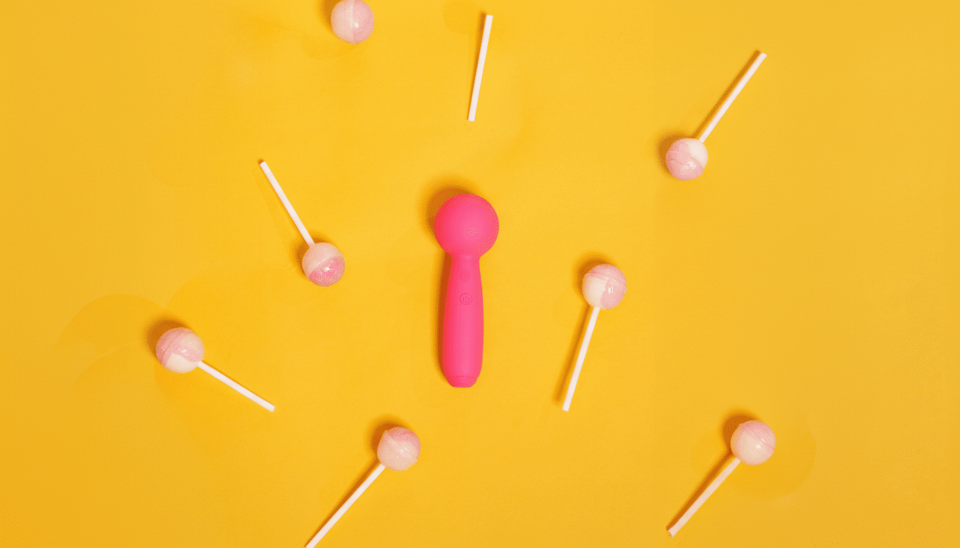 A vibrant yellow background with a pink vibrator in the center, surrounded by several white and pink lollipops scattered around.