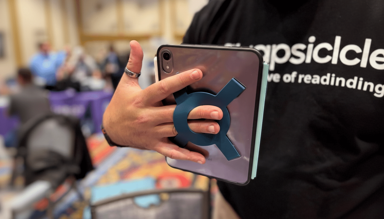 A person holding a tablet with a blue, X-shaped grip accessory attached to the back, showcasing the product in a professional setting.