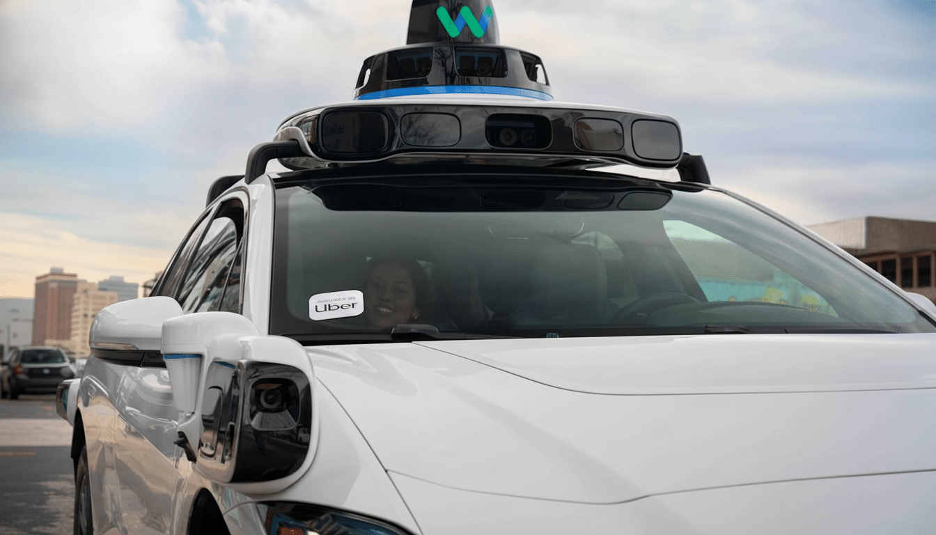 A white self-driving car with a Waymo sensor array on its roof and an Uber sticker on the windshield, with a person visible inside.