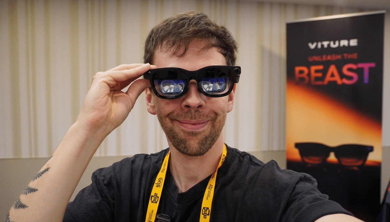 A man wearing black smart glasses, smiling at the camera. The glasses reflect a scene, and a Viture Unleash the Beast banner is visible in the background.