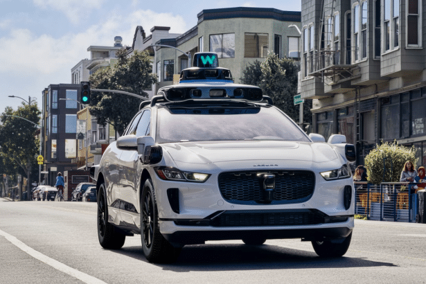A white self-driving car with a W logo on its roof drives down a city street.
