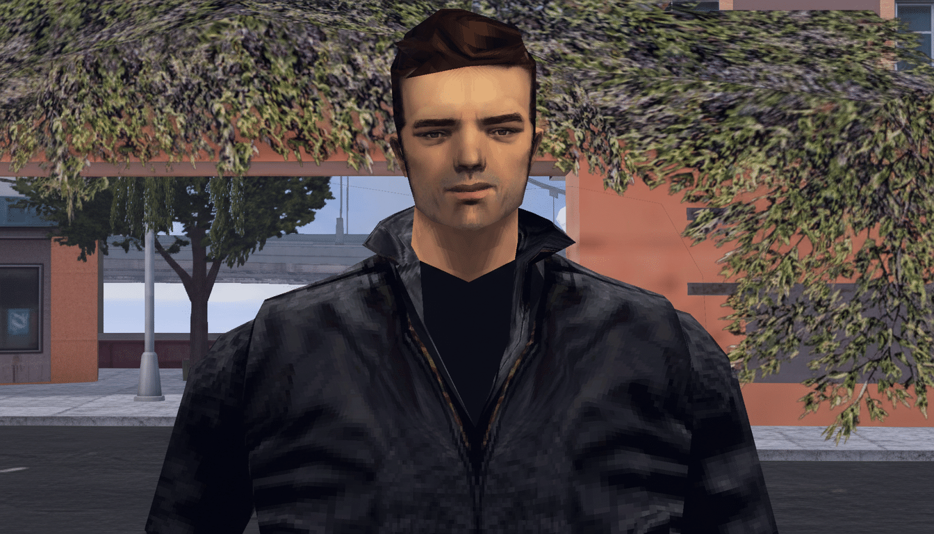 A man with dark hair and a black jacket, standing outdoors with trees and buildings in the background, resized to a 16:9 aspect ratio.