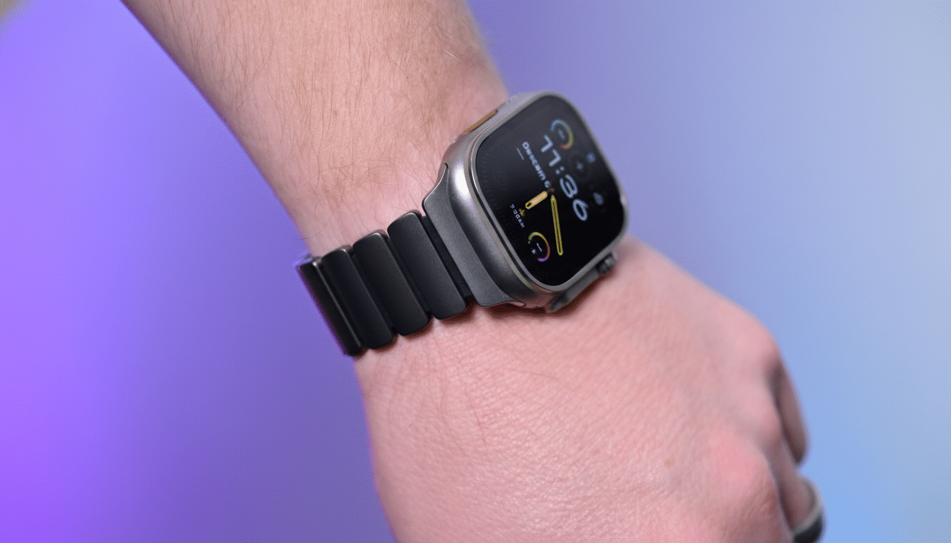 A close-up shot of a persons wrist wearing a dark gray smartwatch with a metallic band, set against a blurred background with purple and blue hues.