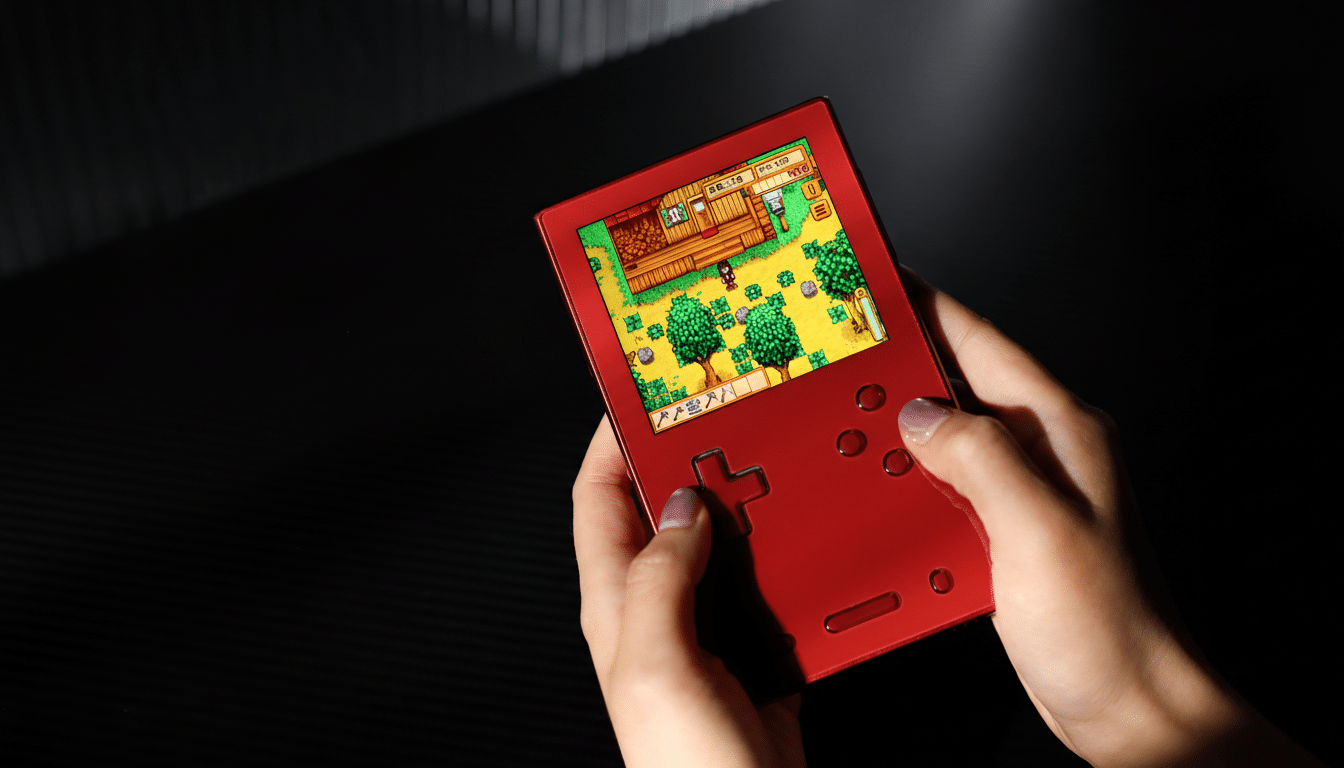 A persons hands holding a red handheld gaming device, playing a pixelated farming simulation game.