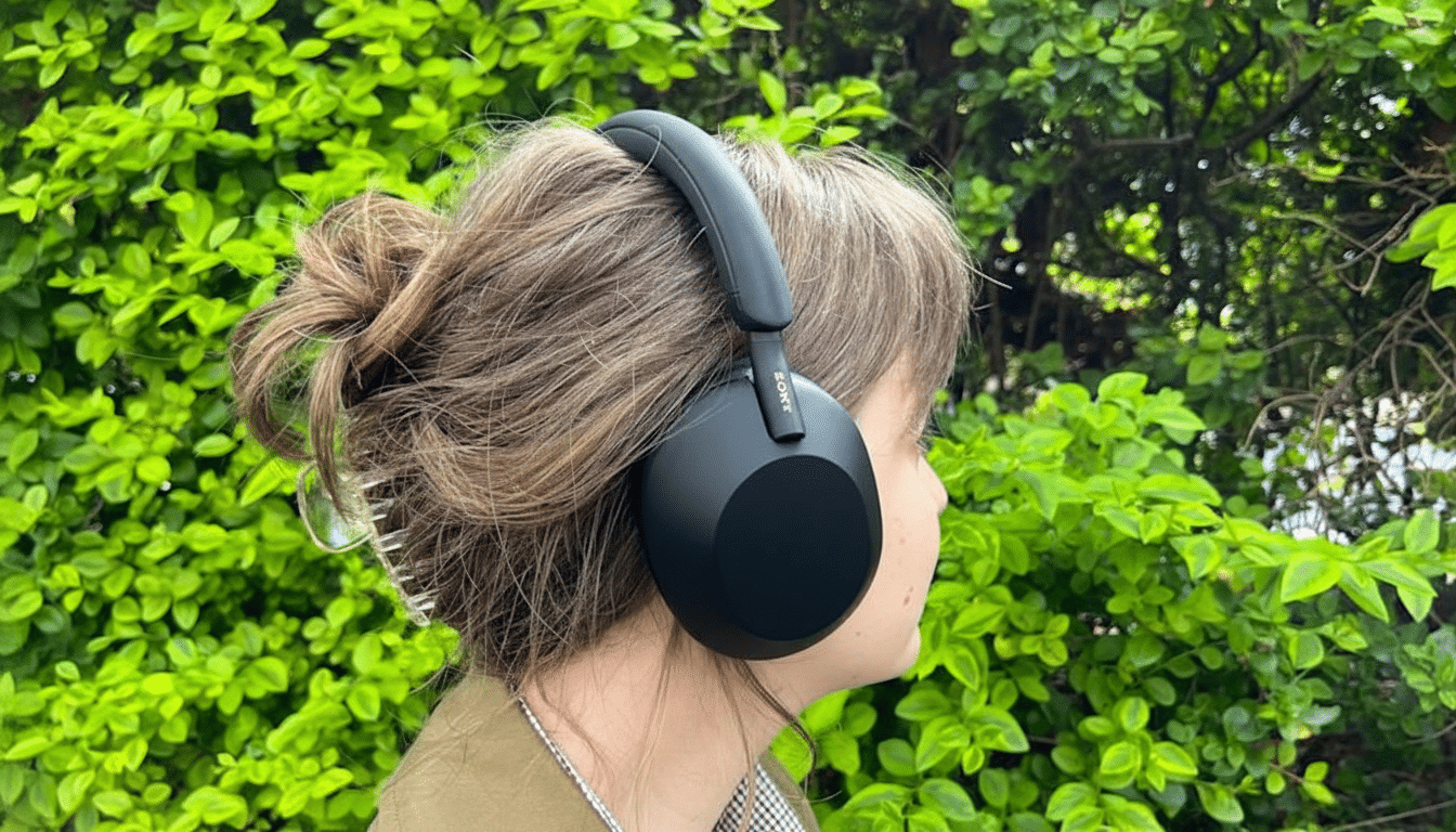 A person wearing black Sony headphones, with their hair in a bun, against a background of green foliage.