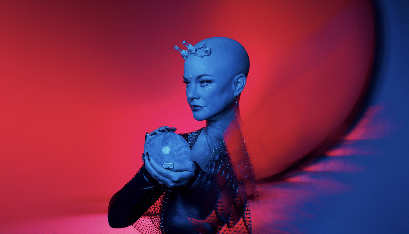A woman with blue skin and a bald head, wearing a black studded top, holding a glowing orb, against a red and blue background.