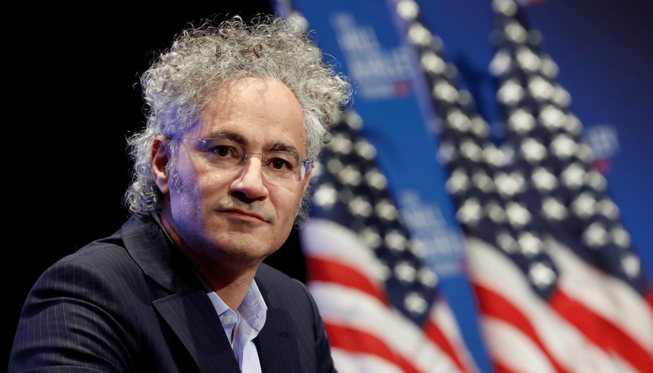 A man with curly gray hair and glasses looks directly at the viewer, with blurred American flags in the background.