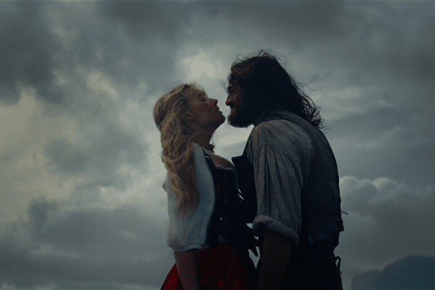 A man and a woman, silhouetted against a cloudy sky, are about to kiss.