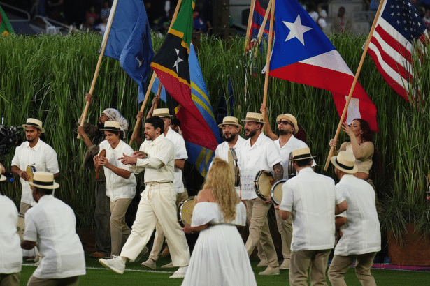 A group of people, some holding flags and others playing drums, are performing on a grassy field.
