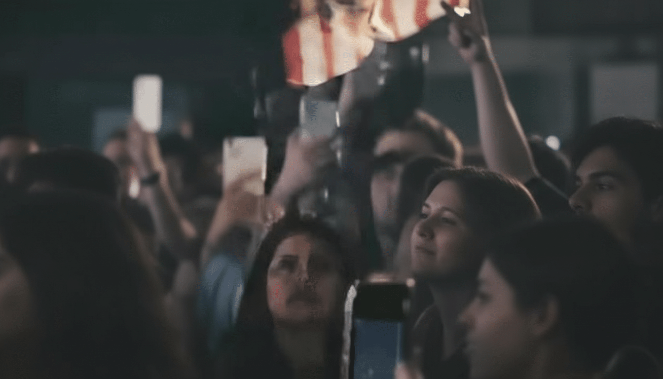 A crowd of people at an event, with some holding up phones and one person holding a red and white striped item.