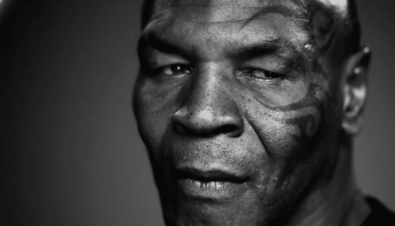 A black and white close-up portrait of Mike Tyson, looking directly at the viewer with a serious expression.