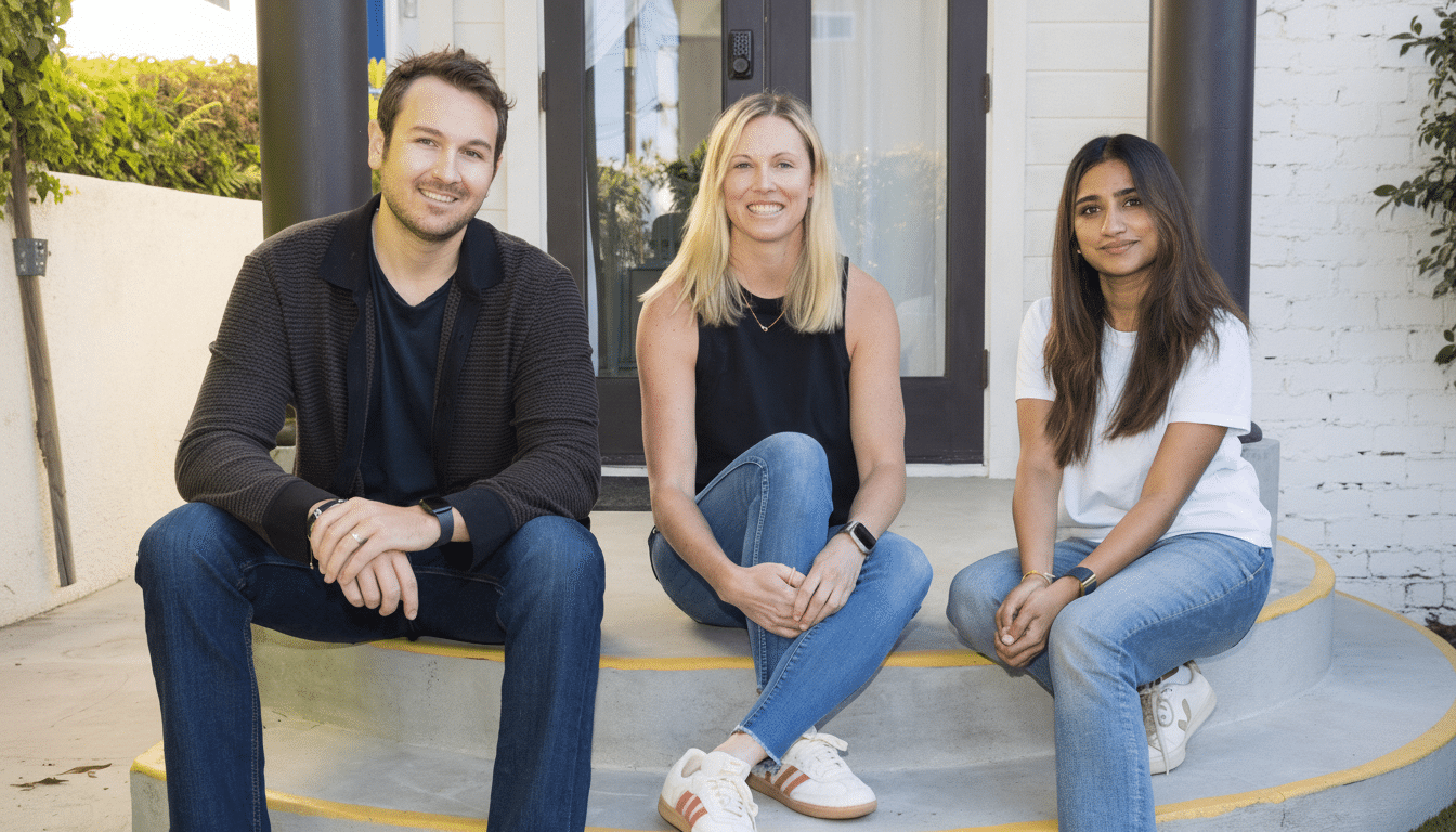 Three people, two women and one man, are sitting on concrete steps in front of a house. The man is on the left, wearing a dark patterned jacket and jeans. The woman in the middle has blonde hair and is wearing a black top and jeans. The woman on the right has dark hair and is wearing a white t-shirt and jeans. All three are smiling at the camera.