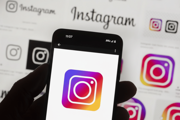 A hand holding a smartphone displaying the Instagram logo, with various Instagram logos and text in the background.