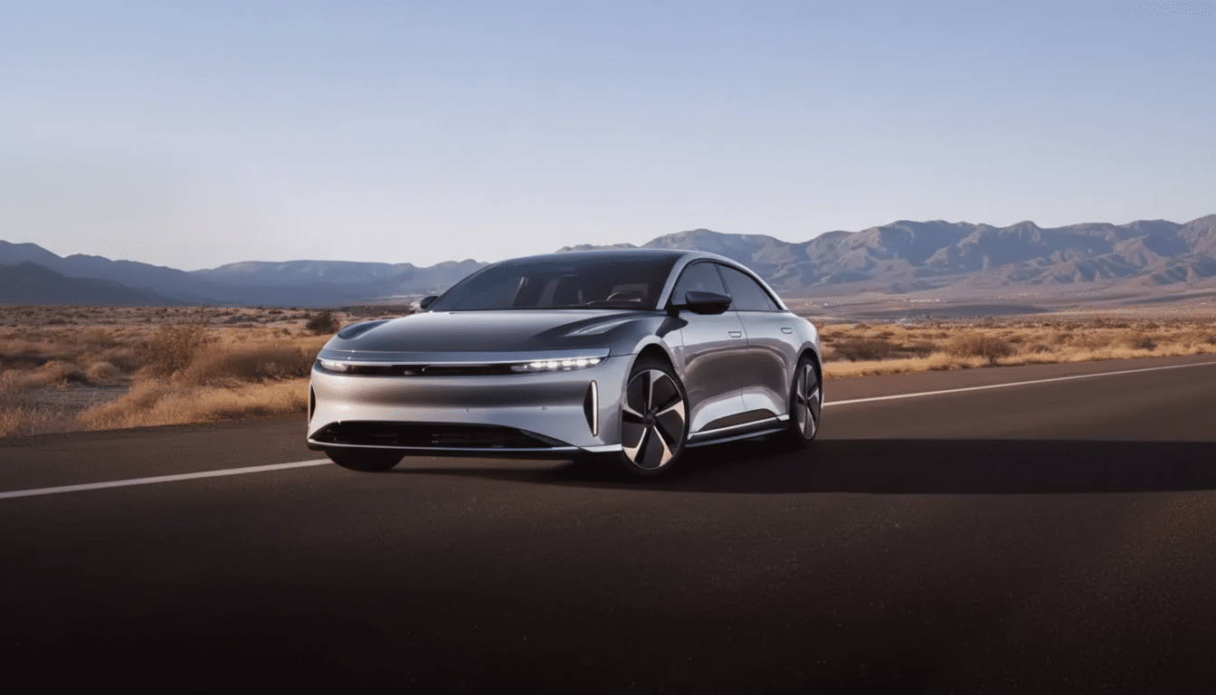 A silver Lucid Air electric car is parked on a desert road with mountains in the background under a clear sky.