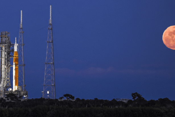 A rocket on a launchpad with a large, orange full moon in the night sky.