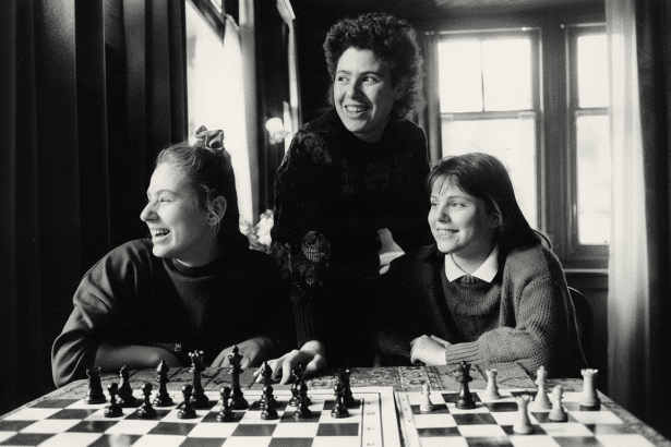 Three young women are gathered around a chessboard, smiling and engaged in a game.