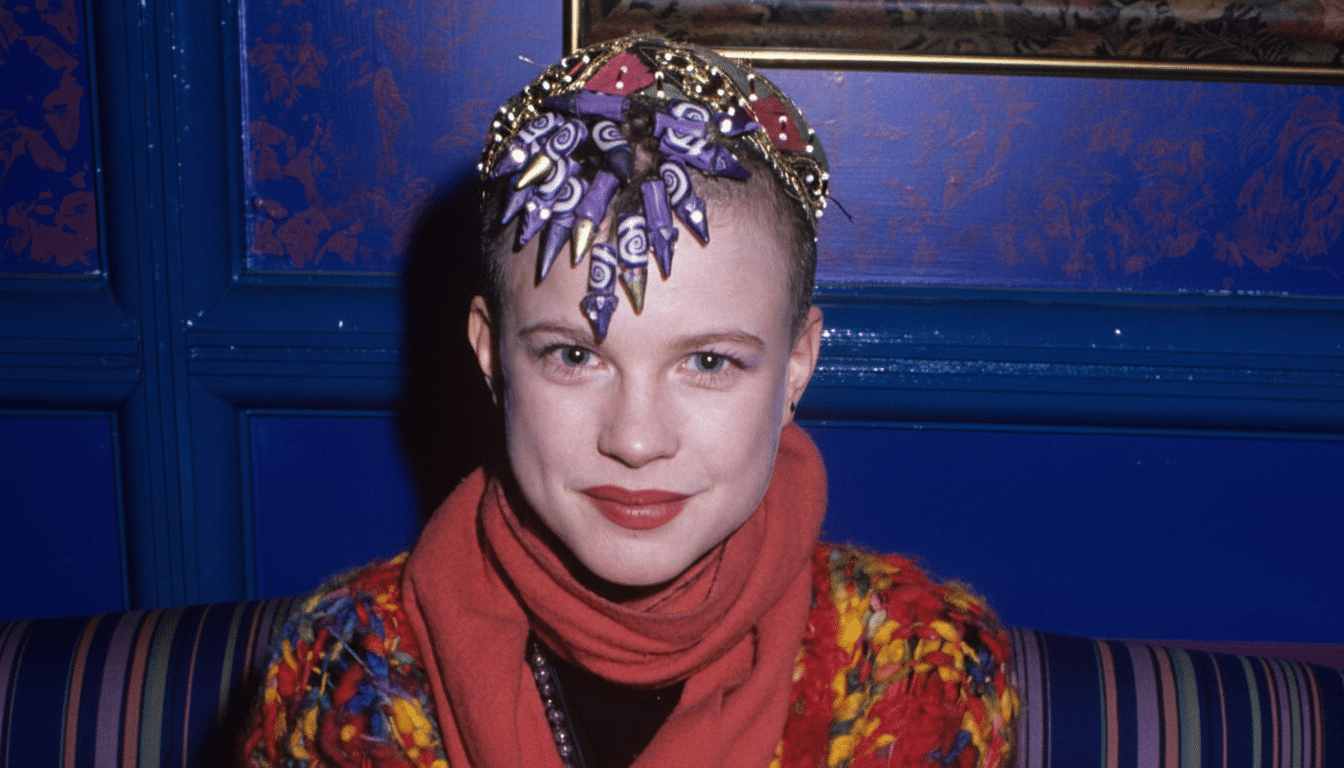 A woman with a unique, ornate headpiece and a colorful outfit, looking directly at the camera.