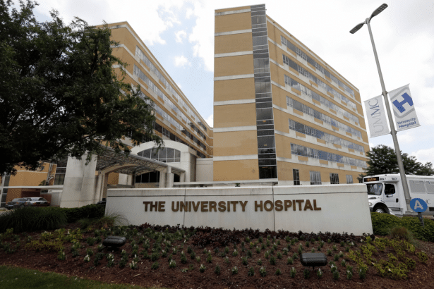 The University Hospital building with a sign in front and a bus parked nearby.