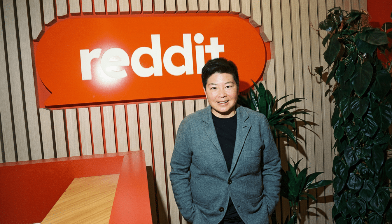 A person stands in front of a Reddit logo, resized to a 16:9 aspect ratio.