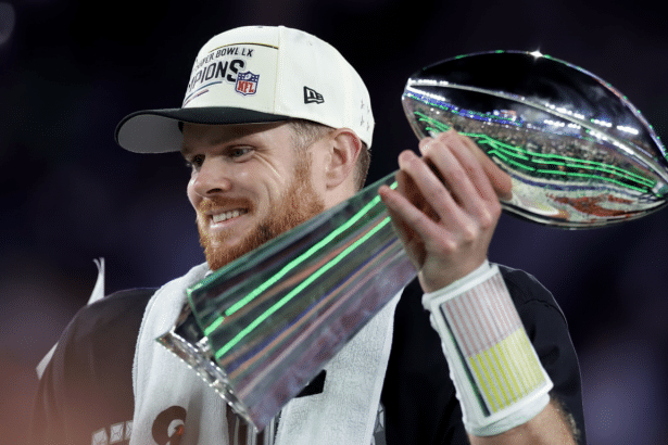 A man with a beard and a white Super Bowl LIX Champions hat smiles while holding a silver trophy.