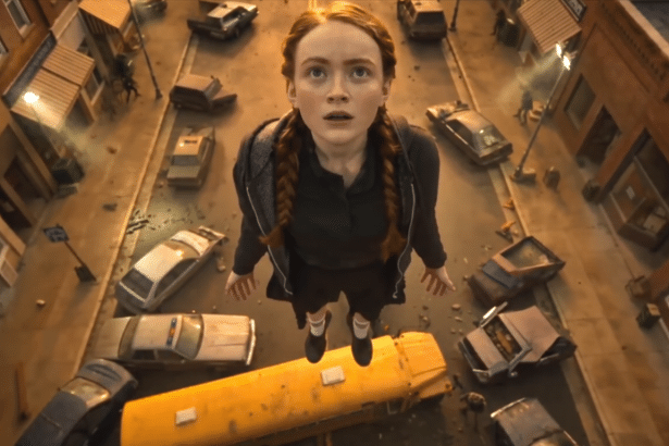 A young woman with braided red hair floats above a street filled with overturned cars and debris, looking up with a surprised expression.