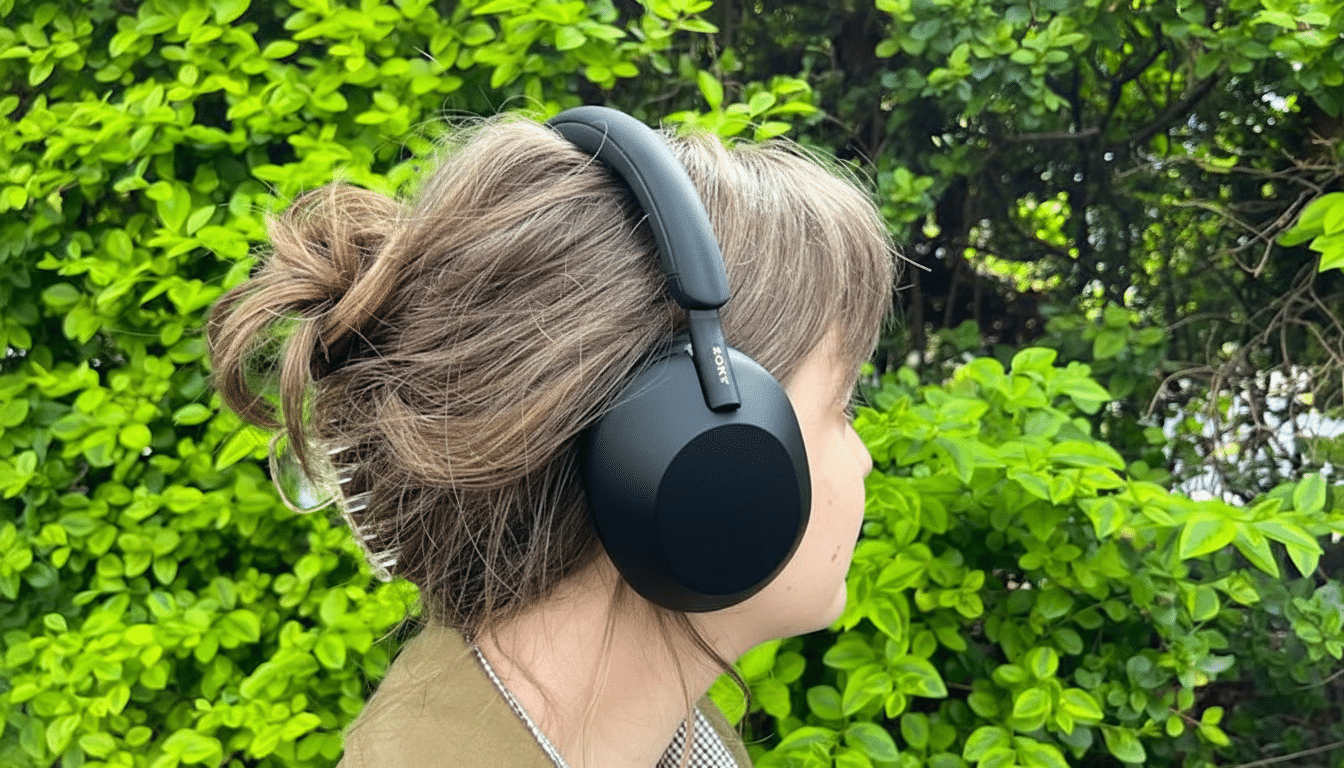 A person wearing black Sony headphones, with a green leafy background.