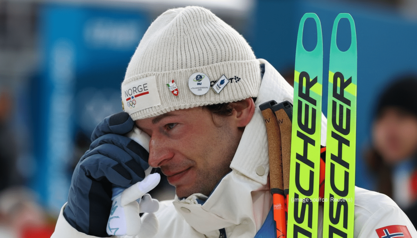 A close-up of a male skier in a white knit hat and jacket, wiping his eye with a gloved hand, with two bright green skis visible on his right side.