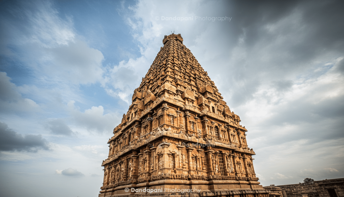 A low-angle shot of the Brihadeeswarar Temple gopuram, showcasing its intricate carvings and towering structure against a dramatic sky.