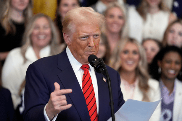 Donald Trump speaking at a podium with a crowd of people in the background.