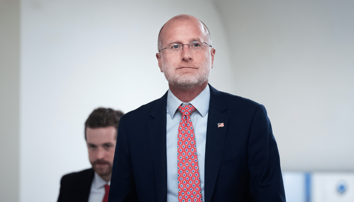 A man in a suit and tie, wearing glasses, looking directly at the camera.