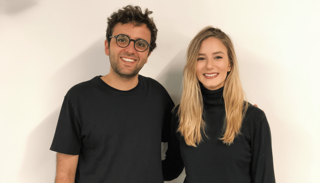 A man and a woman smiling, both wearing black tops, against a white background.