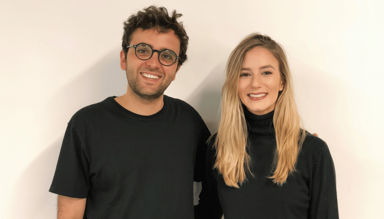 A man and a woman smiling, both wearing black tops, against a white background.
