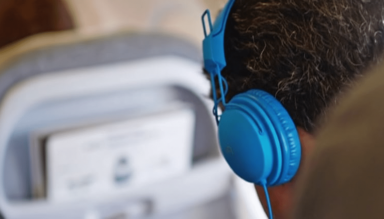 A person from behind wearing blue headphones, with a blurred airplane seat pocket in the background.