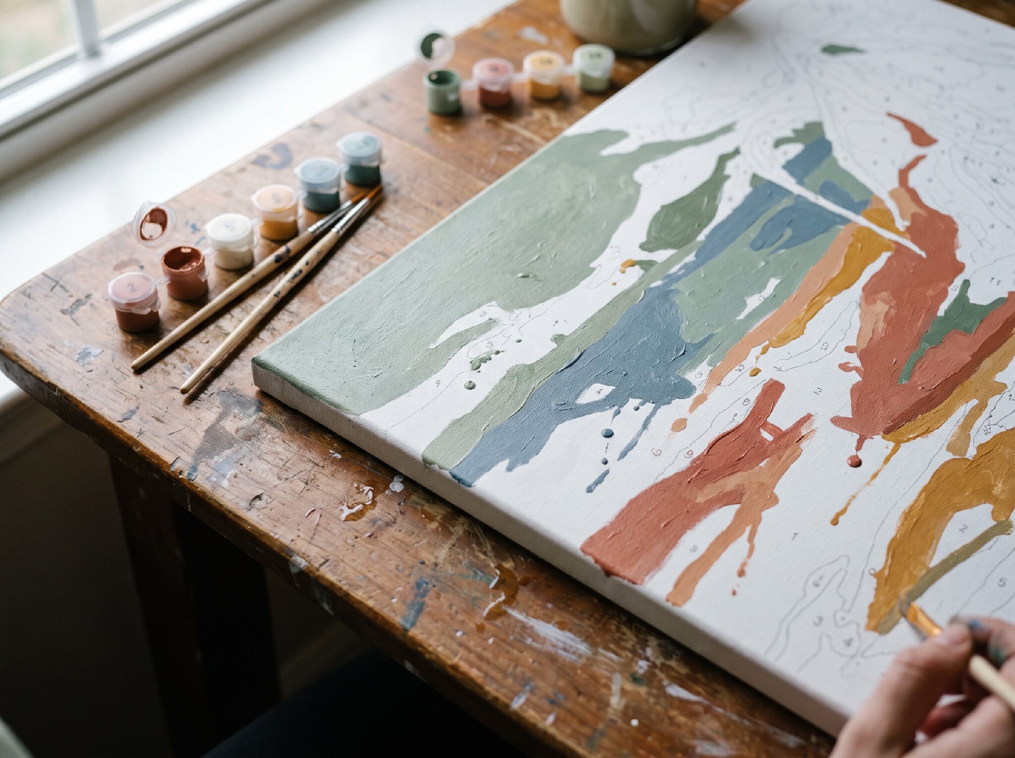 A paint-by-numbers canvas in progress on a table with brushes and paint pots